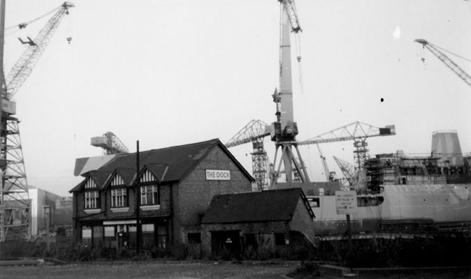 B&W photo of the Dock pub in Wallsend, Tyne and Wear, taken in the late 1980s. A ship and several of the iconic Swan Hunter shipyard cranes tower above the pub.
Andrew Green B&W photo of the Dock pub in Wallsend, Tyne and Wear, taken in the late 1980s. A ship and several of the iconic Swan Hunter shipyard cranes tower above the pub.
Andrew Green